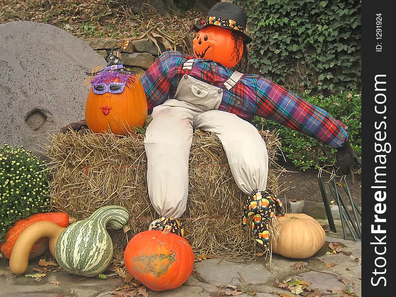 Halloween display with scarecrow, pumpkins, hay and mums.