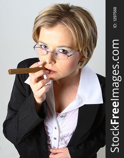 Blond business woman smoking a cigar in front of a grey background