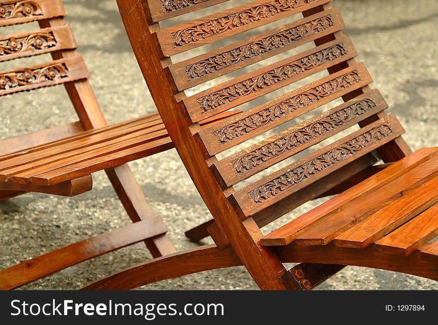 Detail of two decoratively carved wooden chairs sitting in a public plaza. Detail of two decoratively carved wooden chairs sitting in a public plaza.