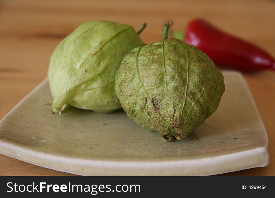 Green tomatillos on a plate with red pepper in background