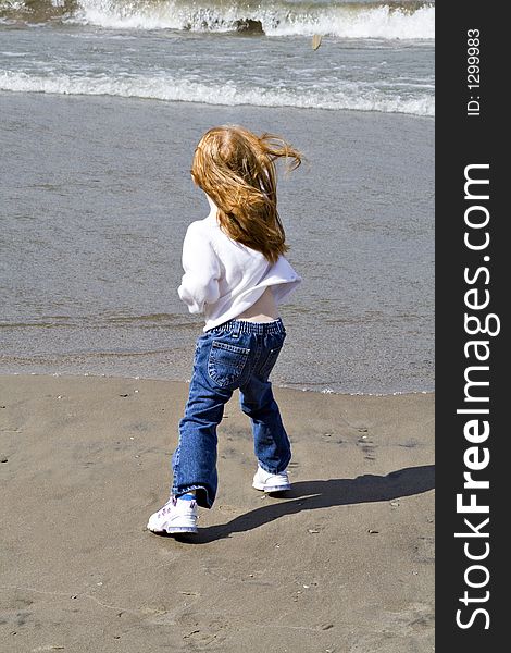 Small red read girl throws rocks into the lake on a windy day. Small red read girl throws rocks into the lake on a windy day.