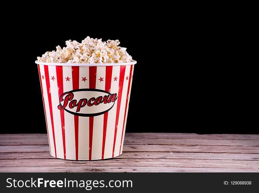 Big classic popcorn in full retro box on wooden rustic desk and black background. Movie and cinema concept. Space for text and design