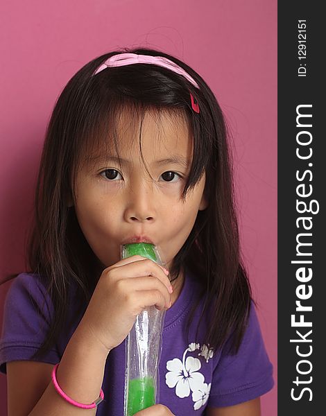 A happy little asian chinese girl eating an green ice pop. A happy little asian chinese girl eating an green ice pop