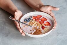 Woman Hands Hold Bowl With Appetizing Healthy Granola Dessert With Pieces Of Strawberries, Cream , Oat Flakes On A Gray Royalty Free Stock Photos