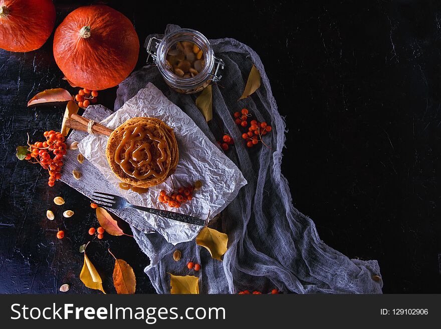 Autumn concept. Pumpkin pancakes with caramel topping, with pumpkins, leaves on a dark background.