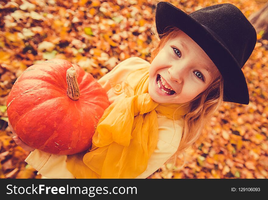 Little beautiful blond girl with big pumpkin in autumn background