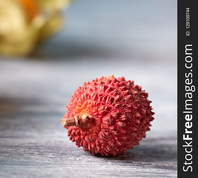 Tropical fresh fruit ripe litchi single on a gray wooden table with place for text. Close-up. Tropical fresh fruit ripe litchi single on a gray wooden table with place for text. Close-up.