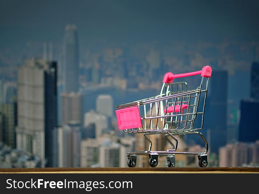 Shopping cart or supermarket trolley on top wooden working table with city and office building background, business and financial concept idea.