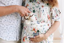 Free Conceptual Photo Of Couples Hands Holding Baby Shoes. Pregnant Woman In Dress On White Background. Pregnancy, Maternity Concept. Stock Photos - 129150743