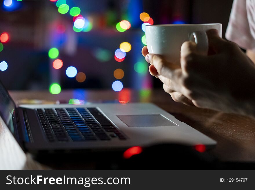 Night time worker in office sitting at the table using laptop and drink coffee f