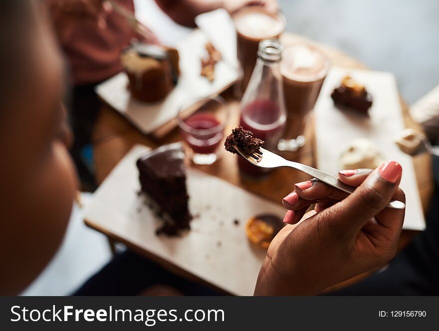 Young woman eating a piece of chocolate cake with a fork while sitting at a cafe table with a group of friends. Young woman eating a piece of chocolate cake with a fork while sitting at a cafe table with a group of friends