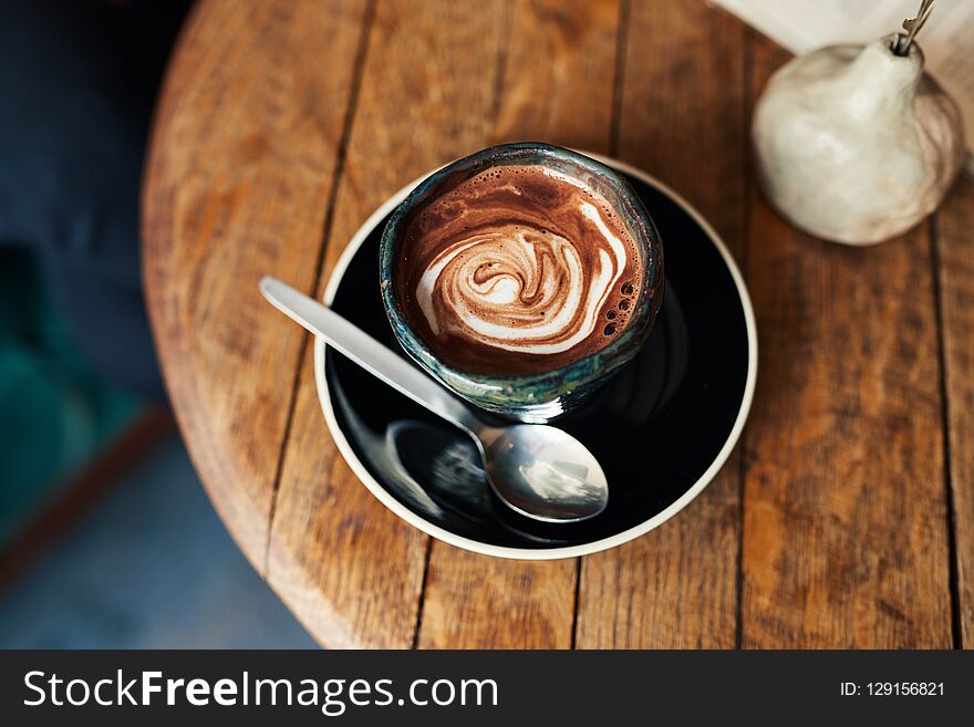 High angle of a delicious latte sitting with a spoon on a wooden table in a cafe. High angle of a delicious latte sitting with a spoon on a wooden table in a cafe