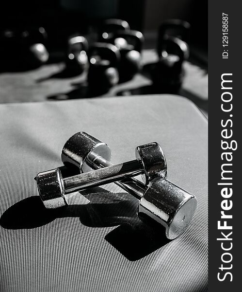 Chrome-plated dumbbells lying on a rubber floor in gym.