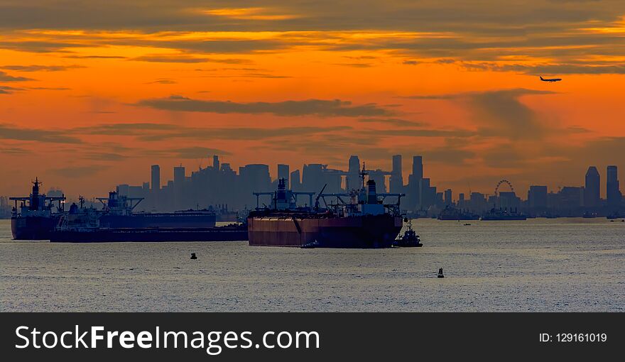 Sunset over Singapore strait with landing airplane and anchored oil tankers and others ship