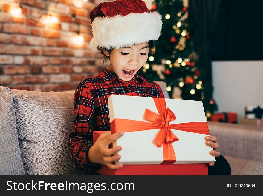 Joyful cute little girl surprised open christmas gift at home. attractive girl childhood with santa hat sitting in living room. open gifts boxing day concept.