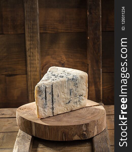 Slice of blue cheese on wooden board on dark background. Studio shot