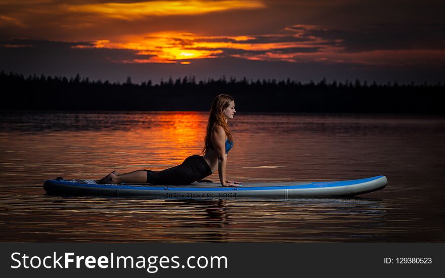 Beautiful slim fit girl with long brown hair exercising yoga on paddleboard in the dark, colorful sunset on scenic lake Velke Darko near Zdar nad Sazovou, Czech Republic. Beautiful slim fit girl with long brown hair exercising yoga on paddleboard in the dark, colorful sunset on scenic lake Velke Darko near Zdar nad Sazovou, Czech Republic.