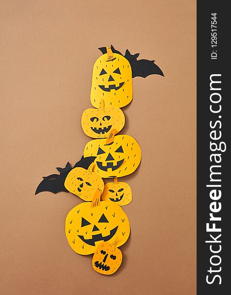 Pattern of paper handcraft pumpkins with scary faces and bats on a brown background with copy space. Composition for Halloween. Flat lay. Pattern of paper handcraft pumpkins with scary faces and bats on a brown background with copy space. Composition for Halloween. Flat lay