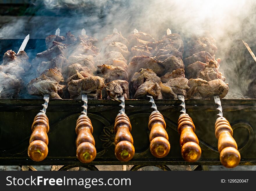 Grilled meat, Golden pork with skewers and wooden handles. A lot of smoke in the process of cooking fragrant meat dishes in nature. Summer kitchen. Raw meat on fire.