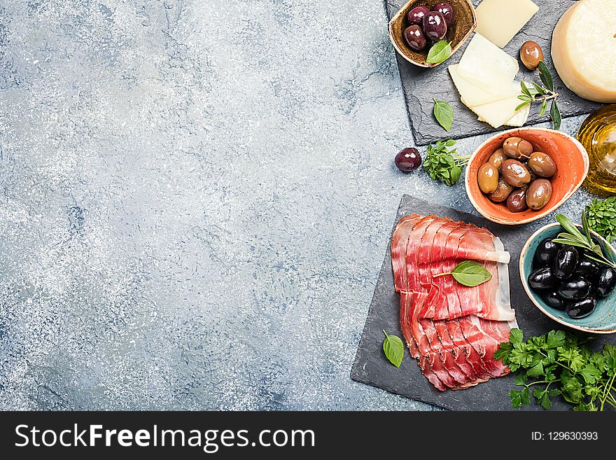 Typical italian antipasto, wooden cutting board with prosciutto, ham, cheese and olives on gray stone background. Top view with copy space