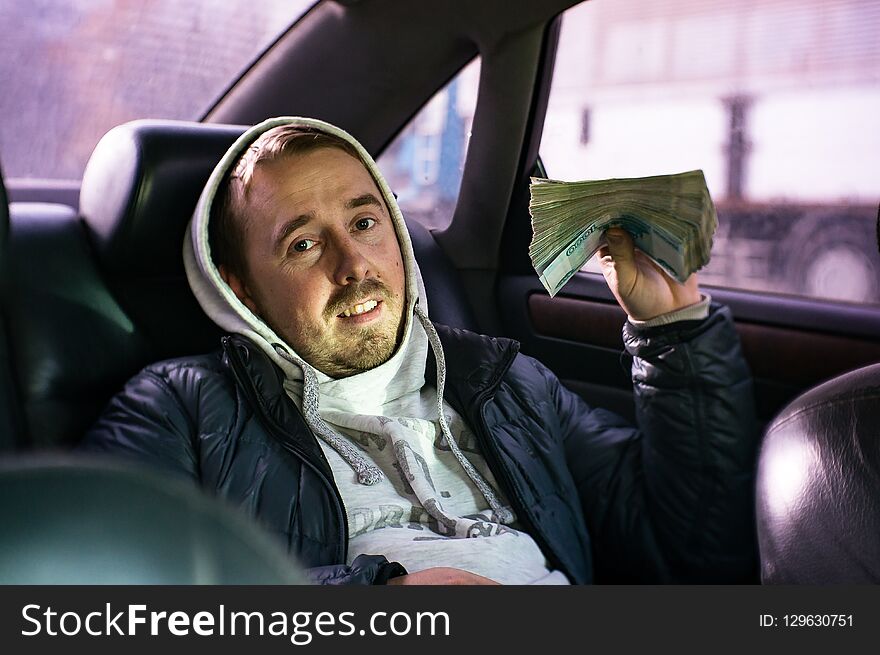 A young man sitting in a car with a big bundle of money.