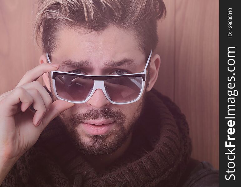 Portrait of a fashion man adjusts sunglasses looking into the camera on a wooden background. Portrait of a fashion man adjusts sunglasses looking into the camera on a wooden background