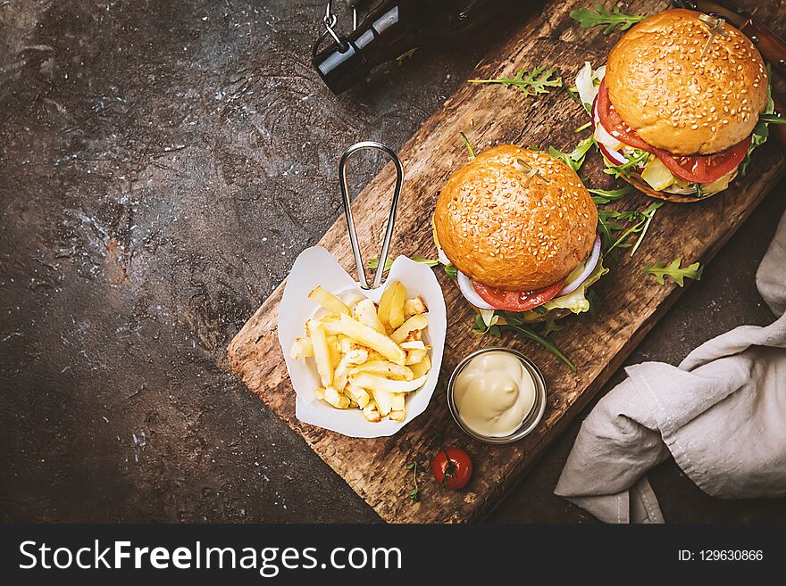 Two tasty grilled classic beef burgers with French fries on a rustic black table, top view with copy space
