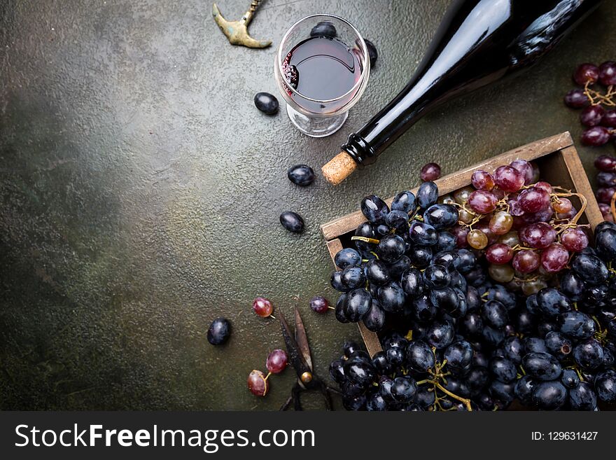 A bottle of red wine with glass and grapes over dark stone background, copy space , top view. A bottle of red wine with glass and grapes over dark stone background, copy space , top view.