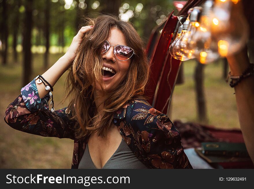 Image of amusing woman 20s wearing stylish accessories smiling while resting in forest camp. Image of amusing woman 20s wearing stylish accessories smiling while resting in forest camp