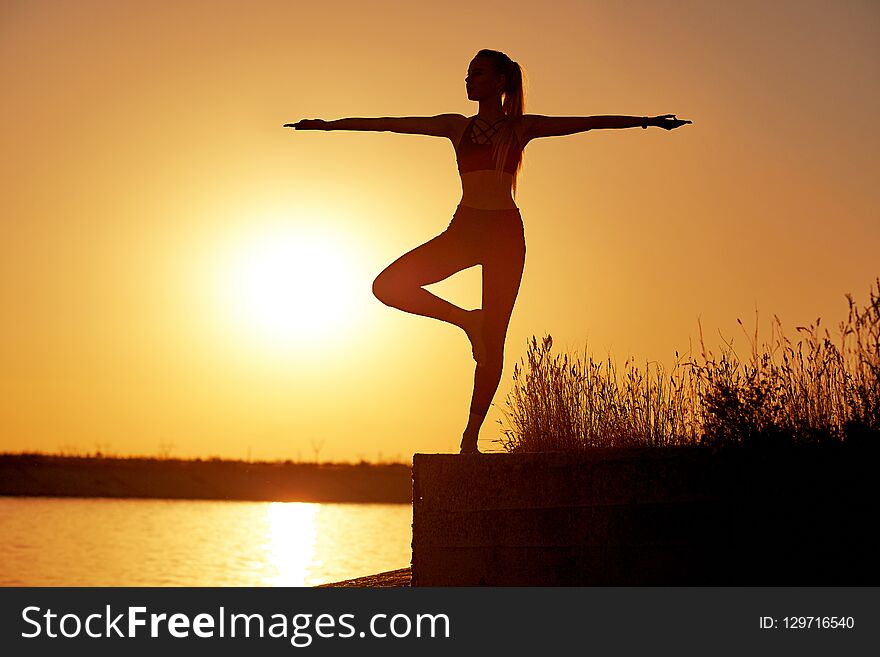 Silhouette woman practicing yoga or stretching on the beach pier at sunset or sunrise