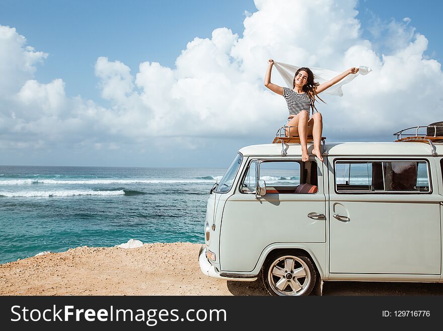 Beauty woman enjoy blow wind with waving white scarf on the retro van roof at the beach