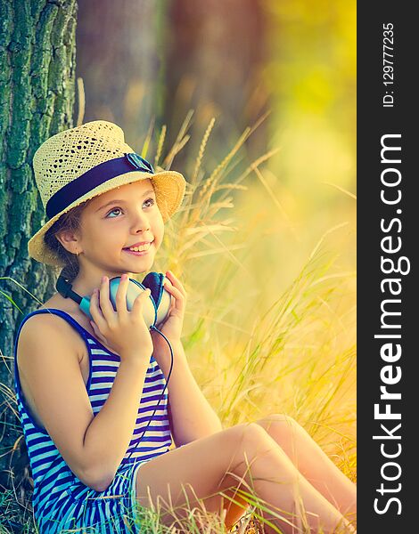 Portrait of the beautiful girl with earphones sitting near the tree