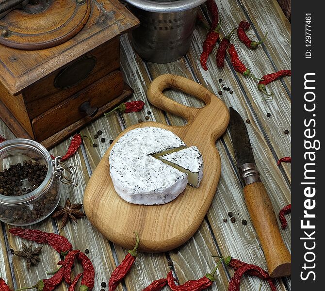 Blue cheese on a wooden board with red peppers, a knife, a coffee grinder