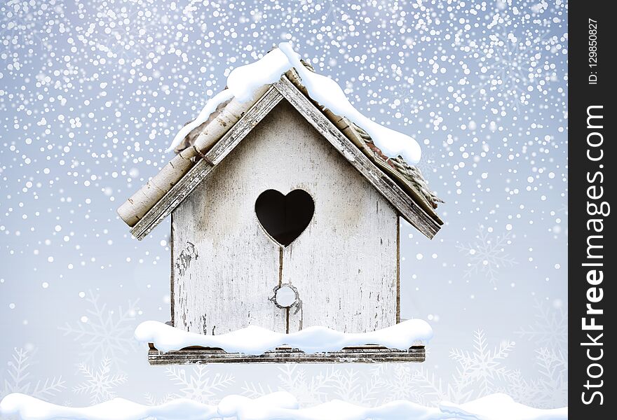 White wooden bird house winter snow falling down on bark roof heart shape
