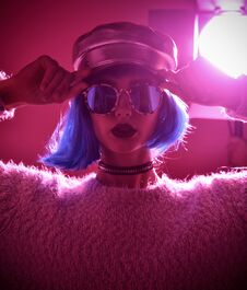 Woman In Fashion Winter Concept Wearing Gold Hat Cap Round Sunglasses In Pink Neon Light Royalty Free Stock Photography