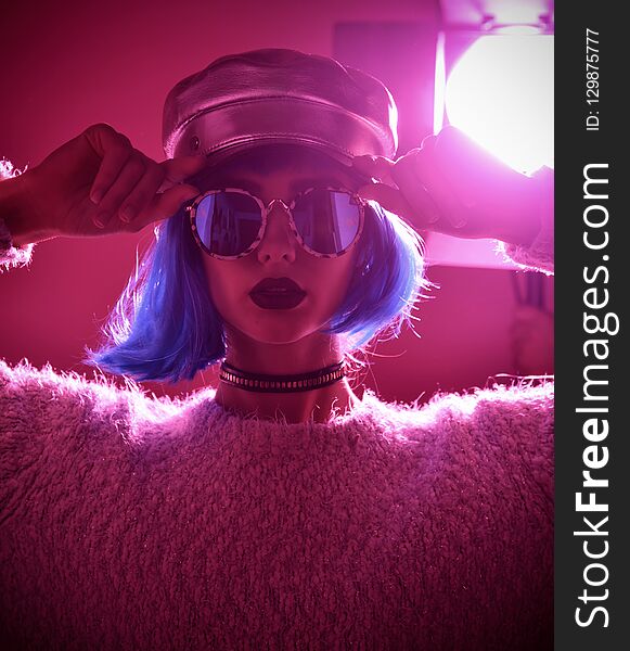 Woman in fashion winter concept wearing gold hat cap round sunglasses in pink neon light