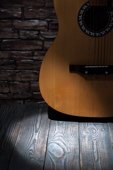 A Beam Of Light In Front Of An Acoustic Guitar Standing By A Brick Wall On Wooden Boards. Royalty Free Stock Images