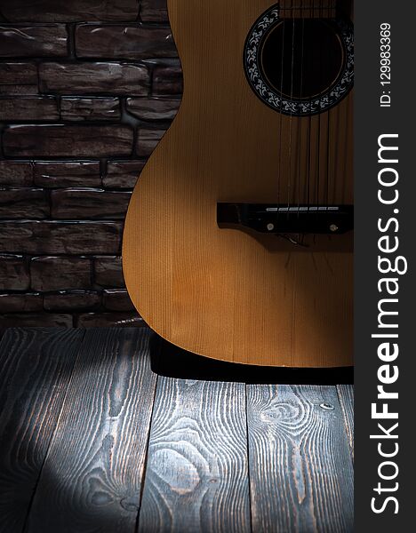 A beam of light in front of an acoustic guitar standing by a brick wall on wooden boards.