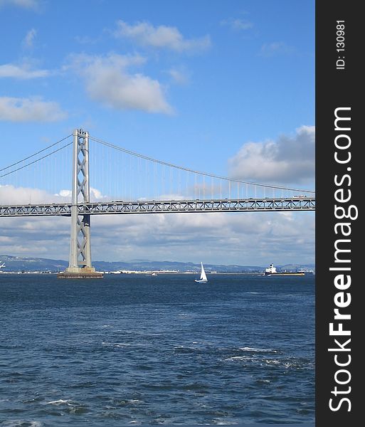 Bright day view of the San Francisco Bay Bridge, with cloud formations. Tall photo with Plenty of sea/water and sky space for titles. Bright day view of the San Francisco Bay Bridge, with cloud formations. Tall photo with Plenty of sea/water and sky space for titles.