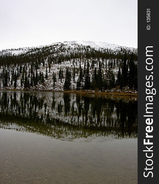 Snowy wooded mountain reflecting in an icy still lake. Snowy wooded mountain reflecting in an icy still lake