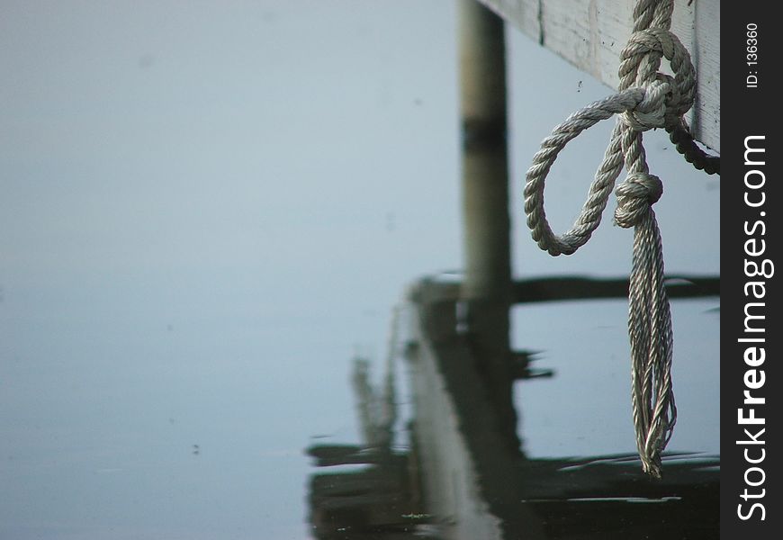 Length of rope, dangling above water, with wooden dock reflected below it. Shallow DOF. Length of rope, dangling above water, with wooden dock reflected below it. Shallow DOF