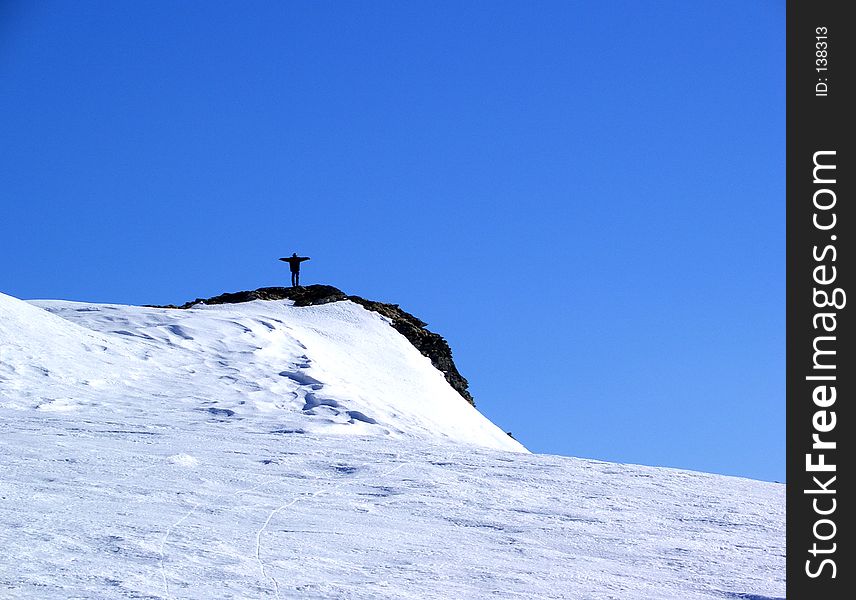 Here is a boy who stand like a cross on the top of the mountain. The winter is very hard and the snow is big.