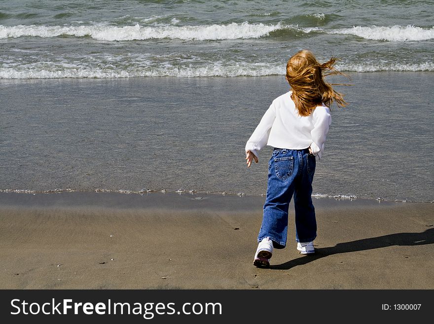 Small red-haired girl playing on the beach - windy day. Small red-haired girl playing on the beach - windy day.