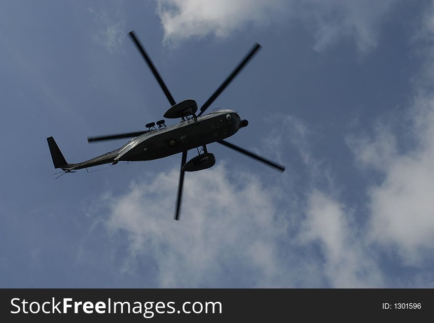 Military helicopter against blue sky with few clouds.