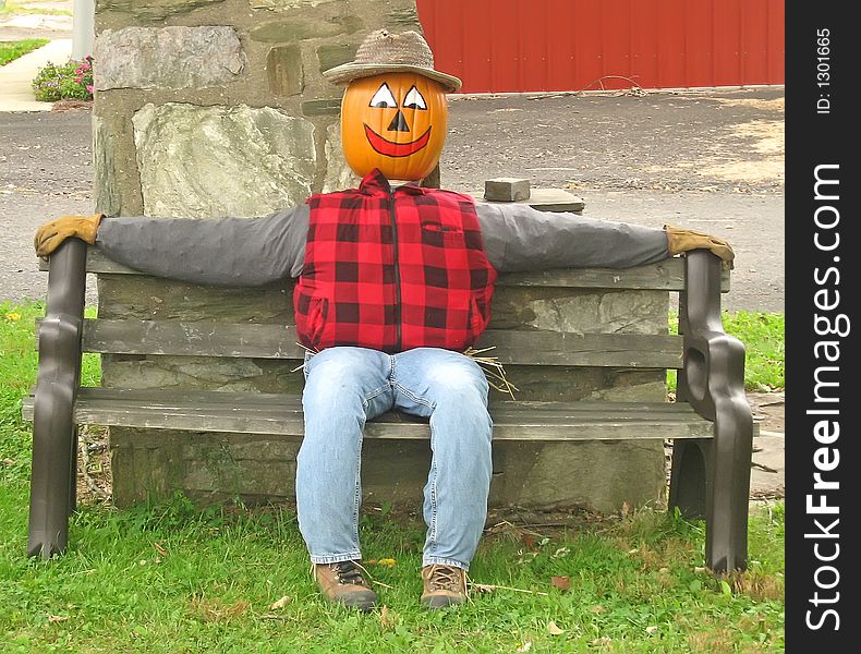 Pumpkin head scarecrow sitting on a bench. Pumpkin head scarecrow sitting on a bench.