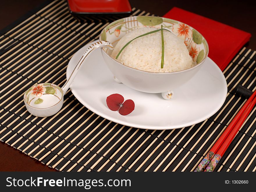 Bowl of rice with chives in antique Asian bowl with chopsticks on a bamboo placemat