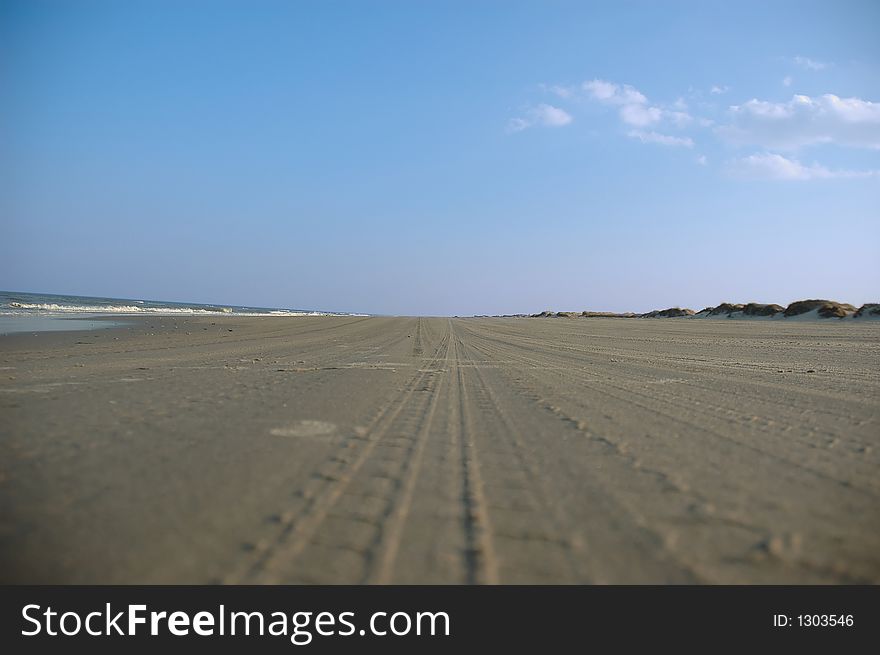 Tire marks embed the beach sand towards the horizon. Tire marks embed the beach sand towards the horizon.
