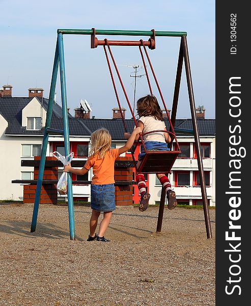 Swinging time; 
girl rocked girl on the swing; 
background city houses and sky