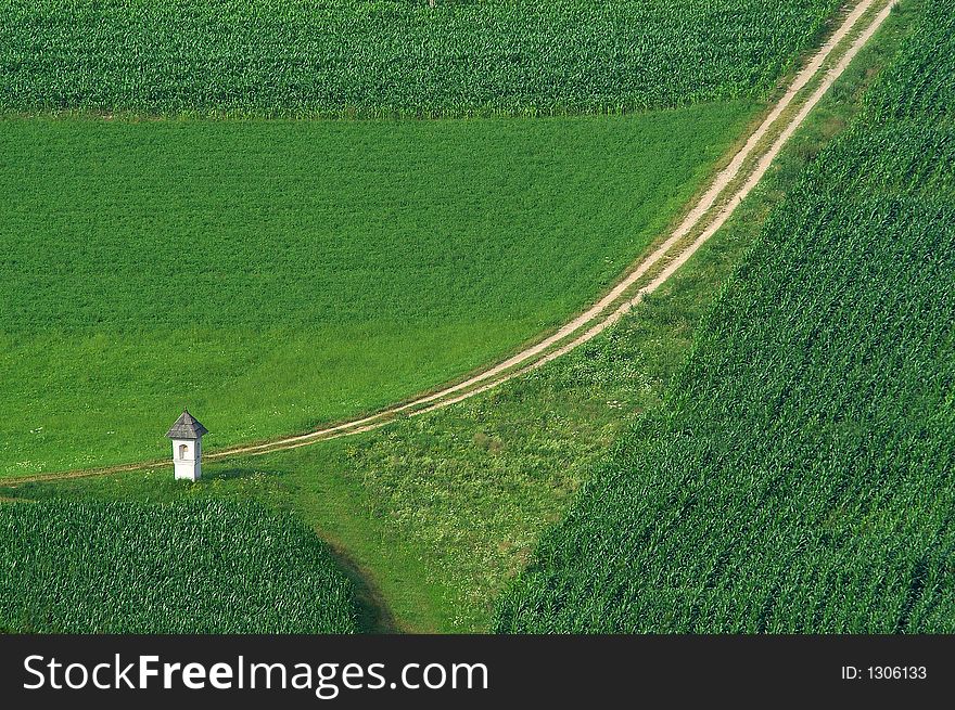 Chapel and path in green field of corn
