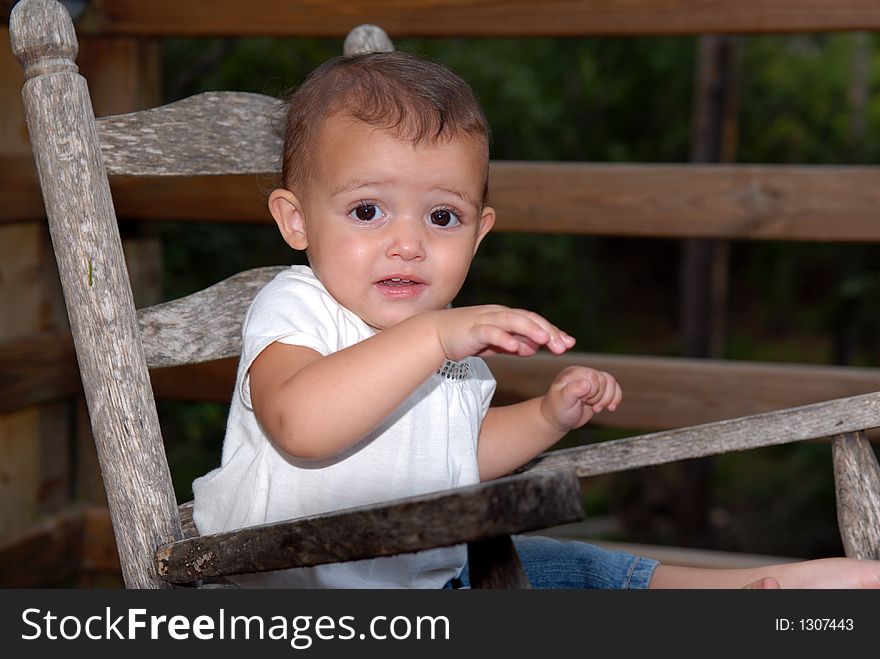 A beautiful little girl with big brown eyes and a sweet expression rocking in an old rocker. A beautiful little girl with big brown eyes and a sweet expression rocking in an old rocker